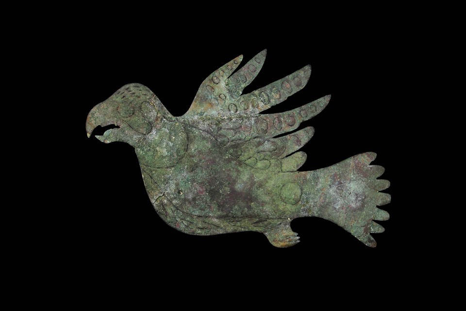 copper falcon A light green-colored cutout of a bird with head to the left, wings on top, feet on bottom and tail to the right on a black background