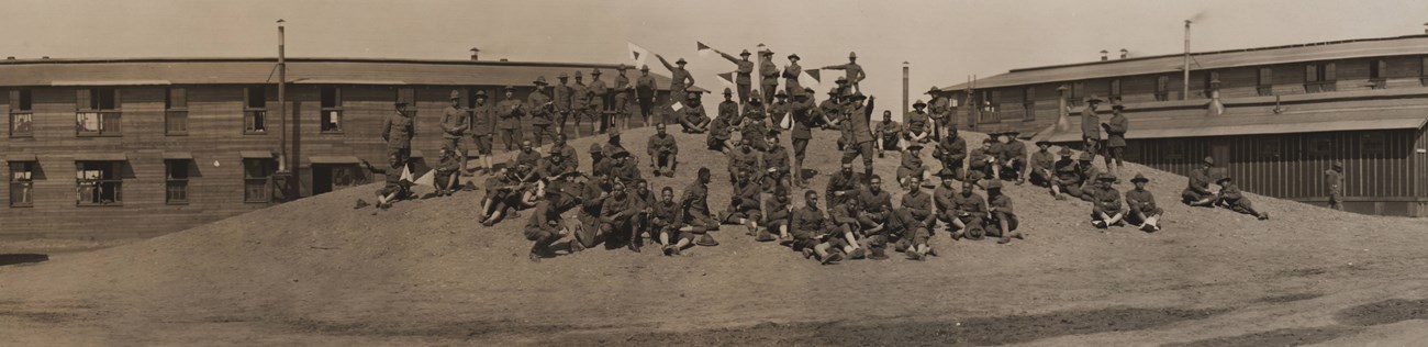 Signal Corp CampSherman2 Several men in uniforms standing and sitting atop a mound of earth between two large buildings