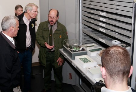 Five people stand in front of a tall steel case with several wide drawers holding artifacts