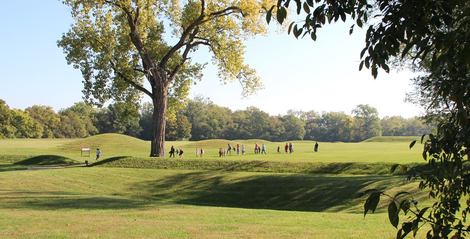 Several people walking around grass-covered mounds