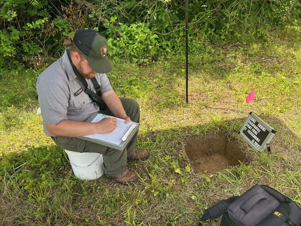 a park archeologist takes notes at an open excavation unit.