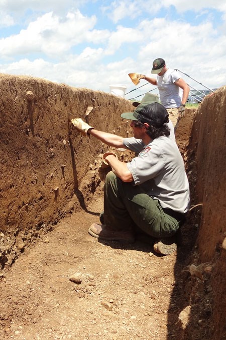 Two workers digging and shoveling in a dirt ditch under a blue sky