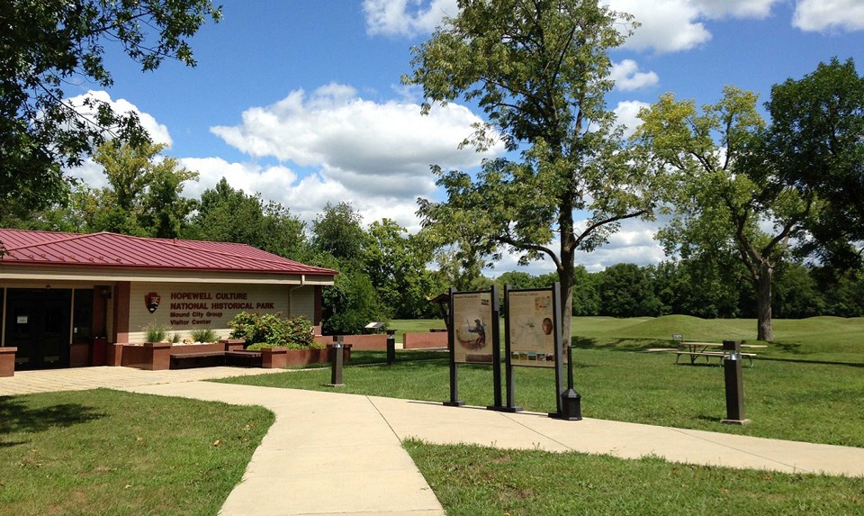 A red-roofed building sits in front of grass-covered mounds in background