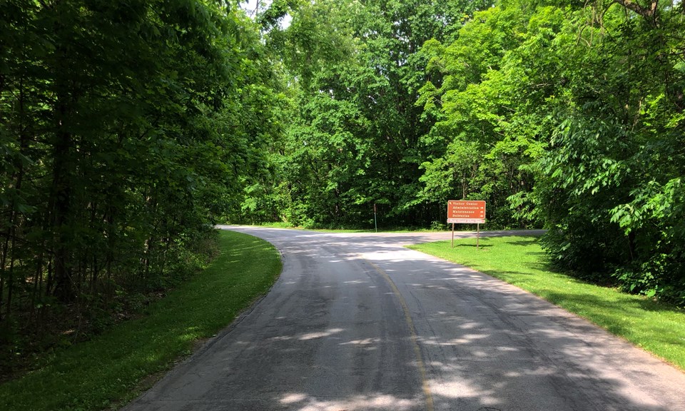 A paved road with green grass on either side and an entrance sign with directions