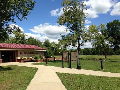 A building with a red roof in front of a grassy-green area with earthen mounds.