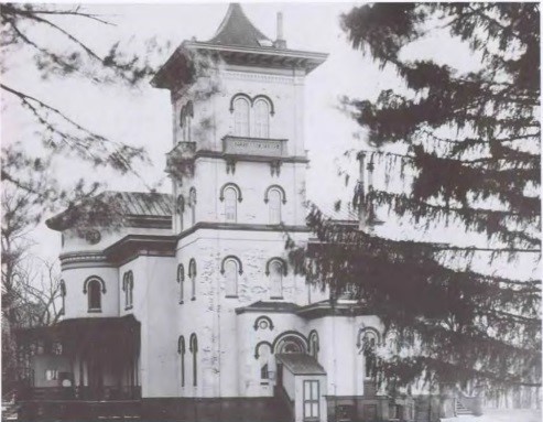 A white, Italianate house with a tower, obscured by trees.