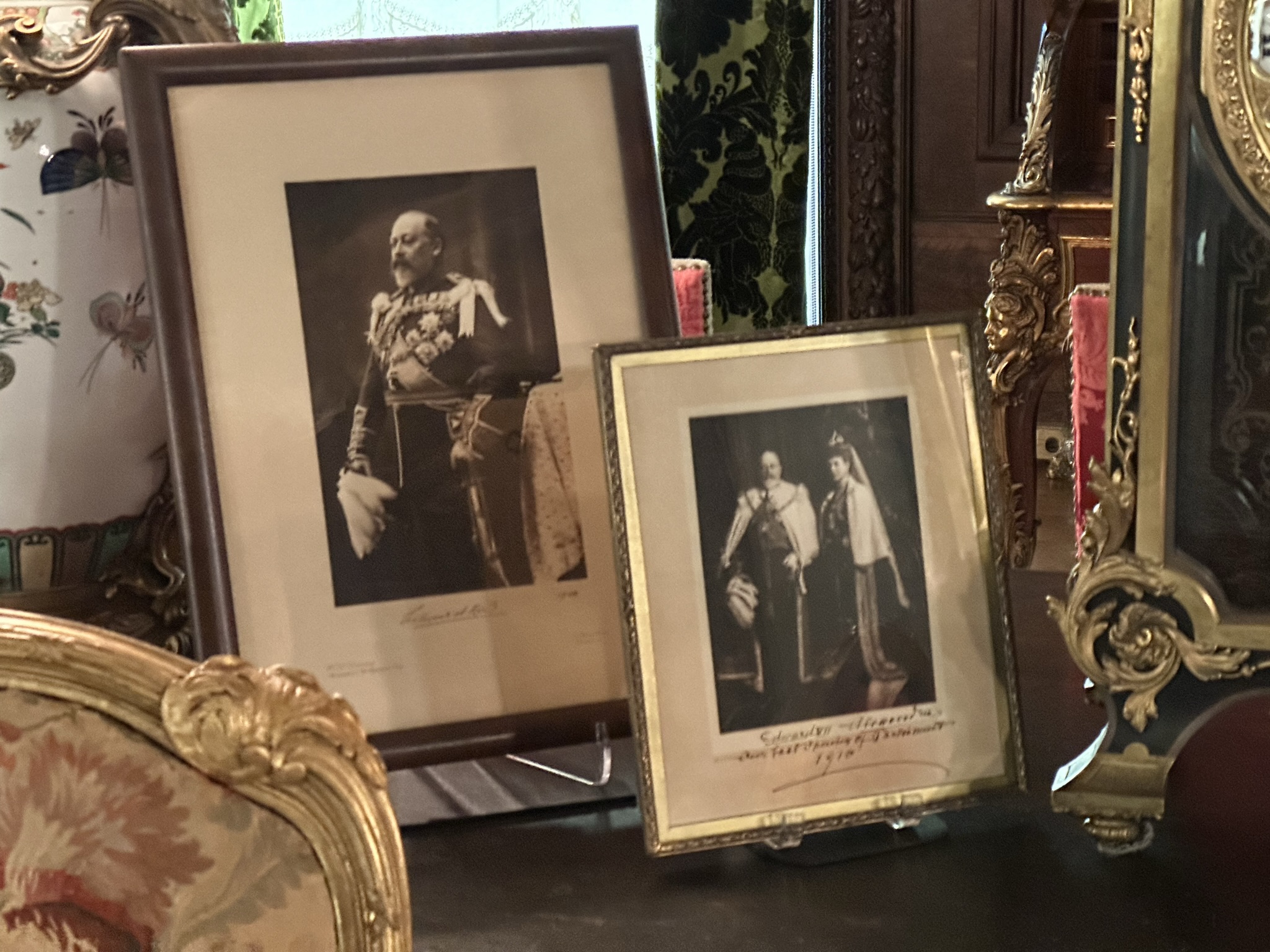 Portraits of King Edward and Queen Alexandria set upon a table in a luxurious furnished room.