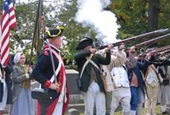 A group of Revolutionary War re-enactors with guns and flag, and costumes.