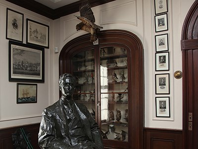 A bronze statue of a man (FDR) in a room surrounded by prints and mounted birds.