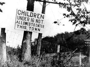A sign attached to a tree stating "children under 16 not allowed to enter this town."