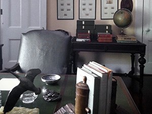 A cluttered desk in a room surrounded by books and pictures.