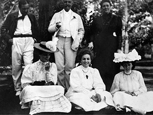 A group of formally dressed people seated and standing on a lawn.