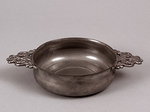 A round metal dish with pierced handles on each side.