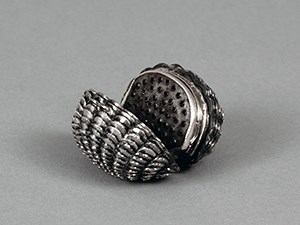 A silver box in form of a clamshell, opened to reveal a pierced grater.
