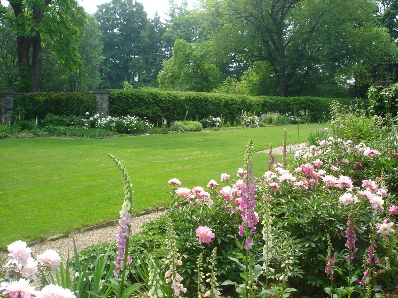 A garden in full bloom surrounding a central lawn of grass.