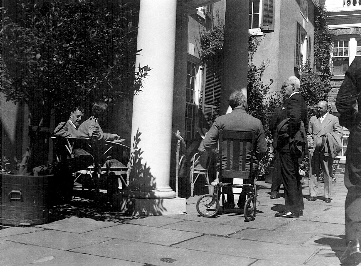 FDR seated in a wheelchair among a group of people on a terrace.