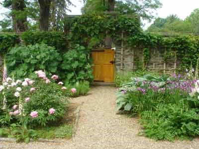 A garden stone wall with garden gate surrounded by lush blooming flowers.