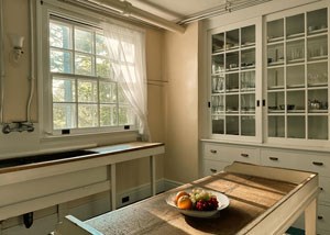 A room with sinke under a window and built-in cupboards along the wall.