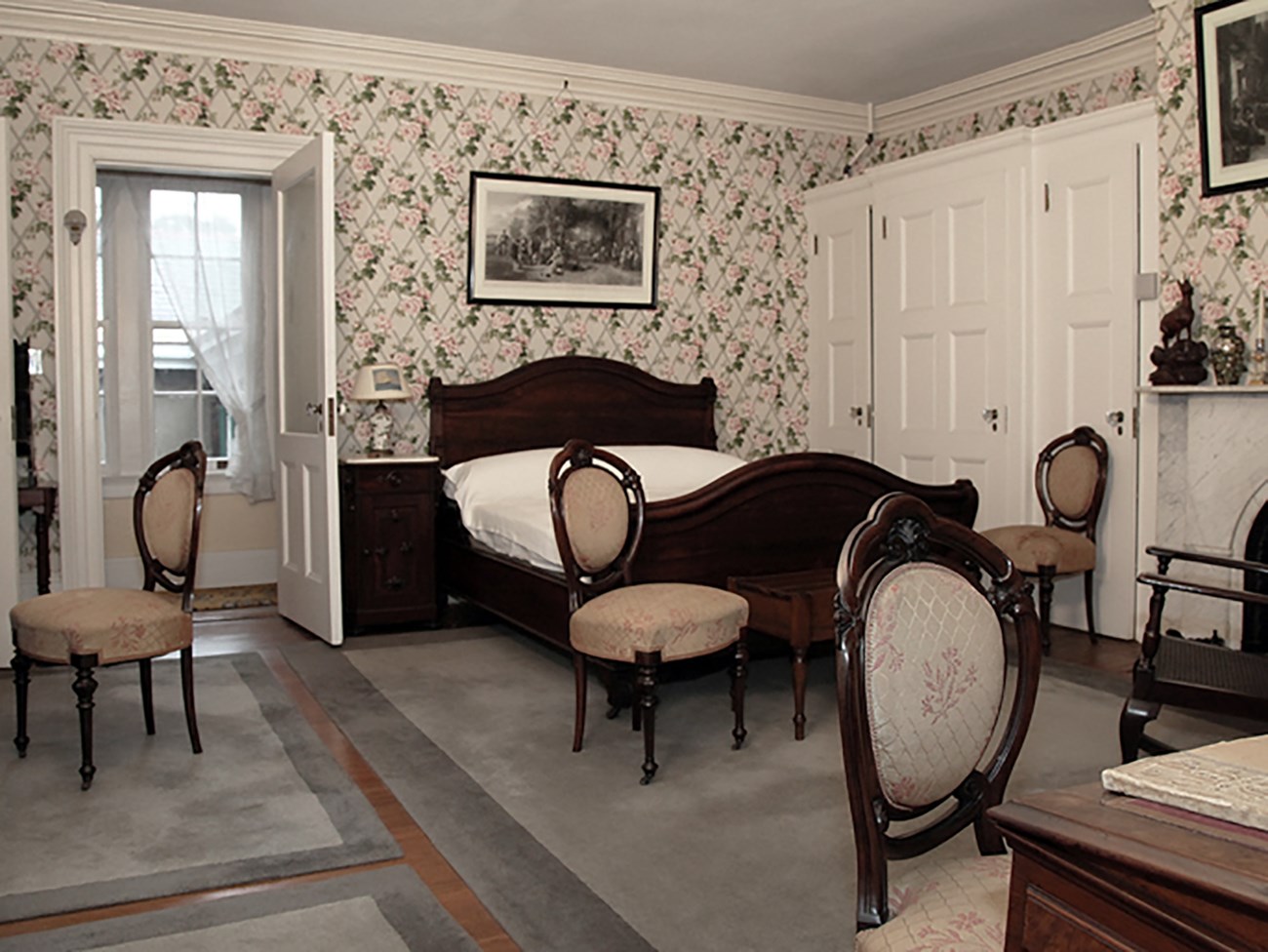 A bedroom with dark wood bed and floral wallpaper.