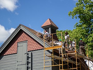 Park Rangers on scaffolding and roof of a wooden building.