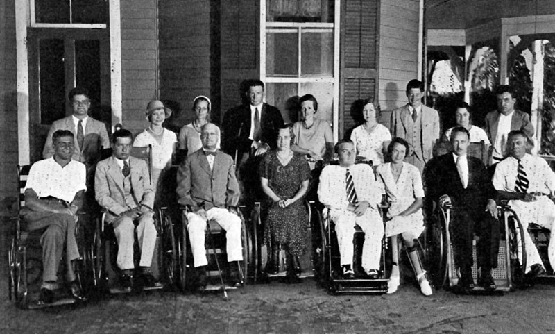 A group of seventeen people posing for a photo, the front row all seated in wheelchairs, the back row standing.