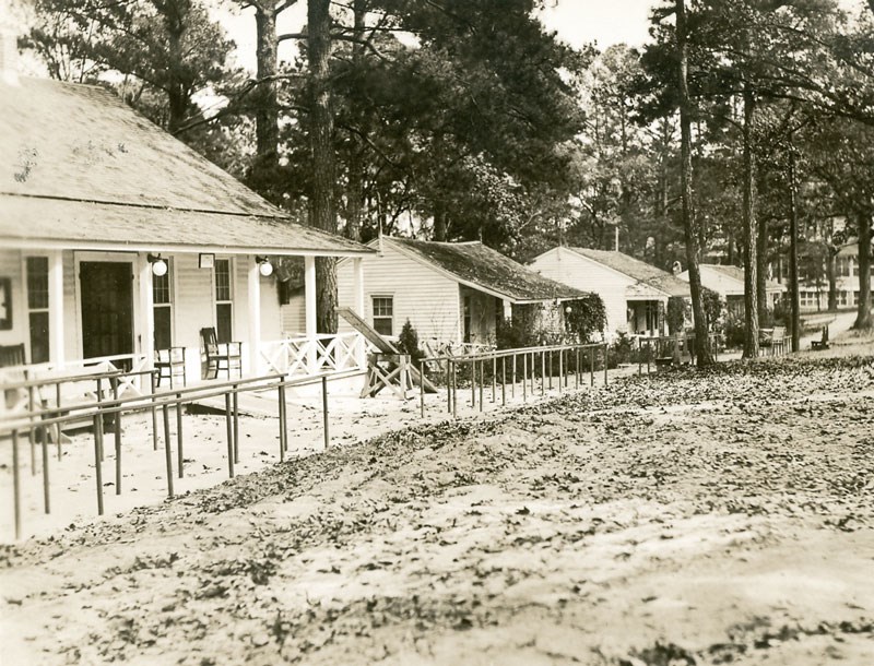 A row of cottages with covered porches with a series of parallel bars along the front lawn.