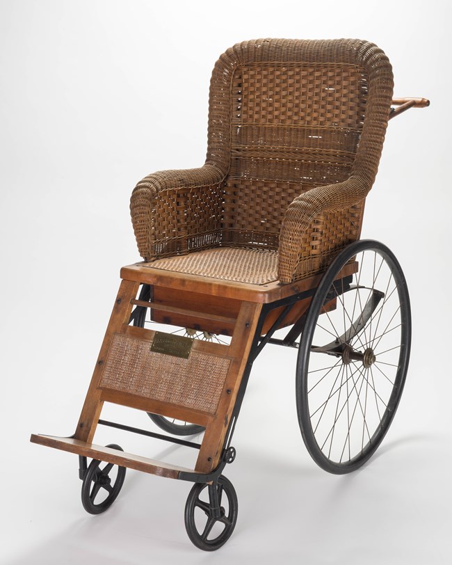 A rattan chair on wheels with push handle on the back