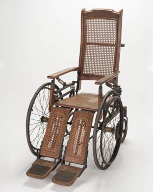A wood wheelchair with caned seat and back.