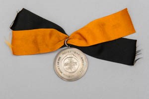 A sterling silver medal with black and gold ribbon in a clasp
