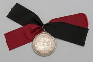 A silver fraternity medal with red and black ribbons