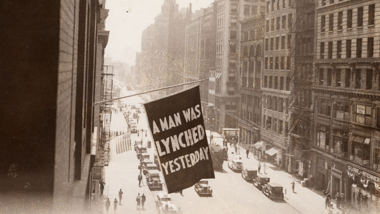 Flag, announcing a man was lynched yesterday, flown from the window of a building on a busy street.