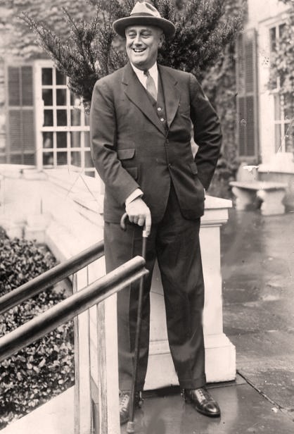 Franklin Roosevelt standing on the terrace at Springwood, supported by a cane.