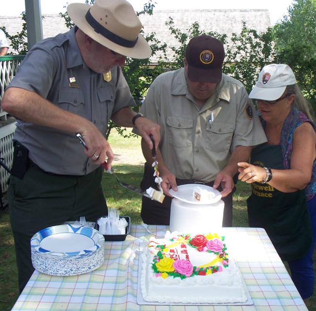 Three people cutting and serving cake including a Park Ranger, volunteer and member of Friends Group