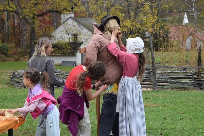A family of four girls assemble a scarecrow using straw.