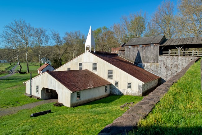 White structure with red roof made of terracotta shingles. Belfry is attached to top of structure. Bridge House in background.