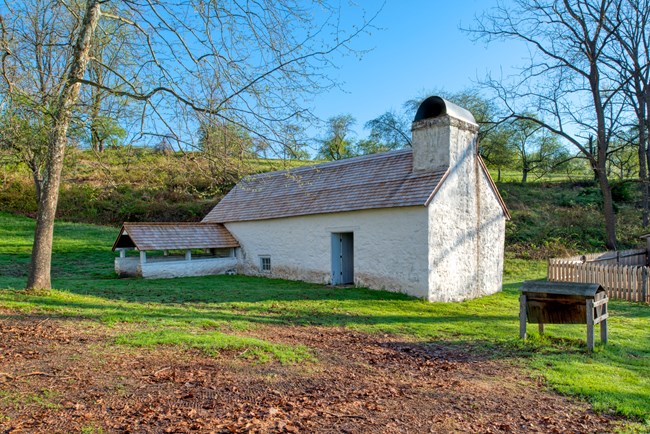 White building built into the ground with chicken feeder in foreground.