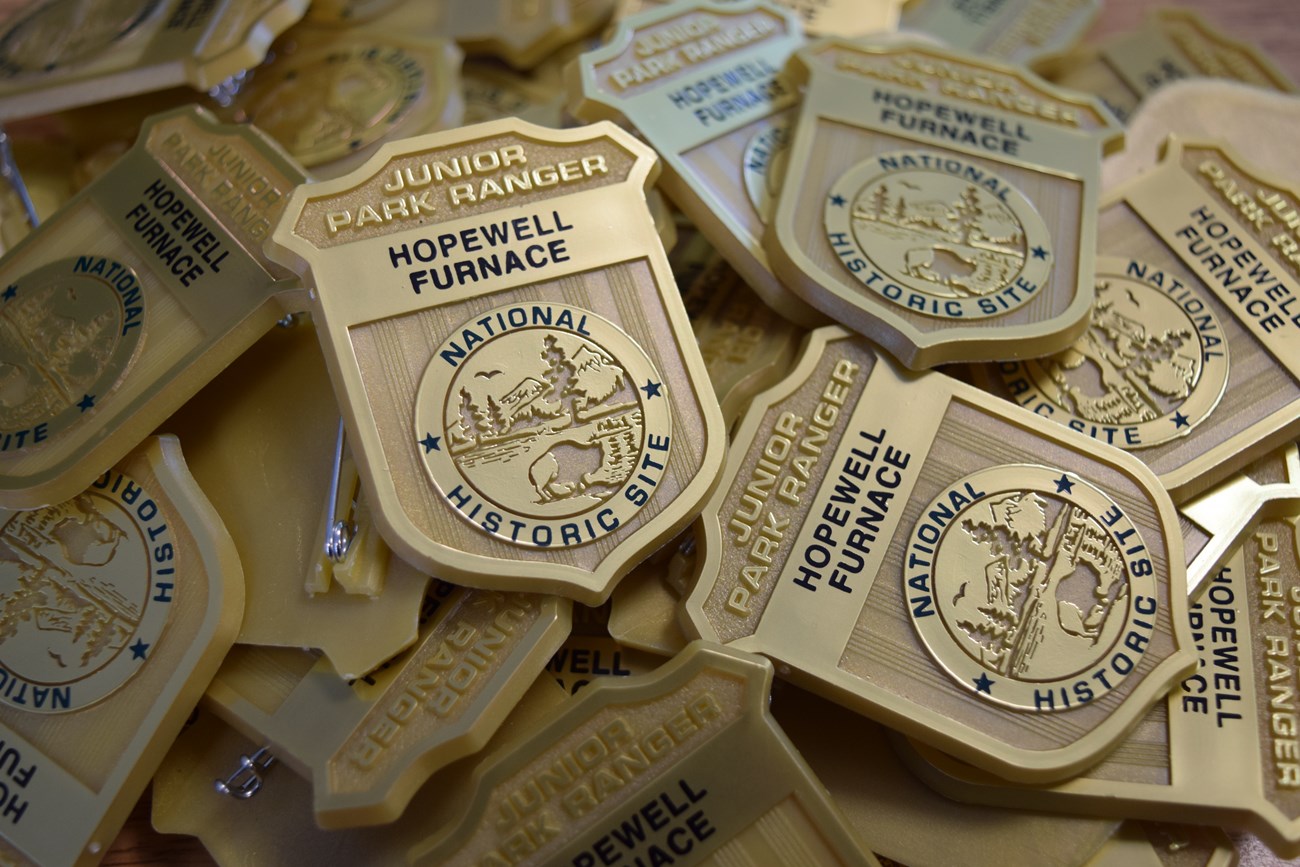 Pile of gold junior ranger badges that say Hopewell Furnace National Historic Site