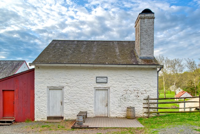 White stone store with red shed to the left. Sign above door reads "Buckley and Brooke Office and Store".