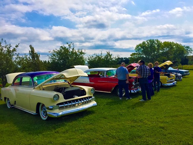 People gather near a row of antique vehicles.