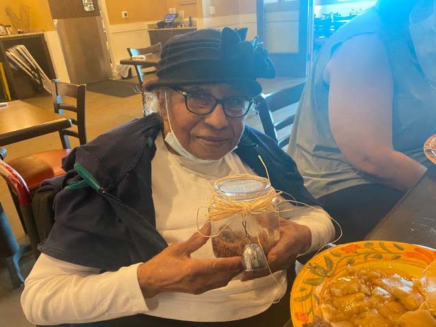 Elderly black woman holds a jar of soil with a bell attached