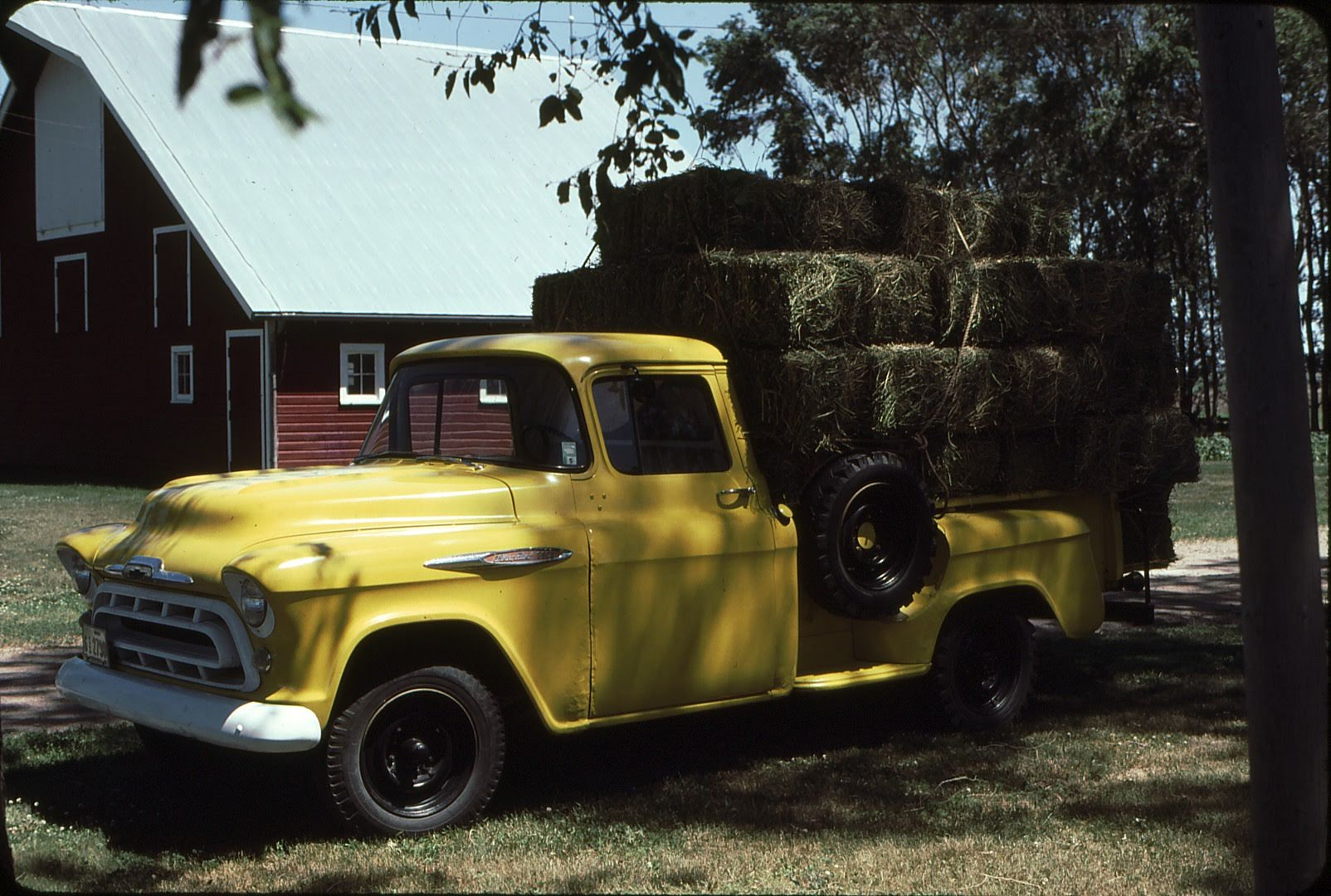 MicrosoftTeams-image (6) Yellow truck with a load of hay parked near a barn.