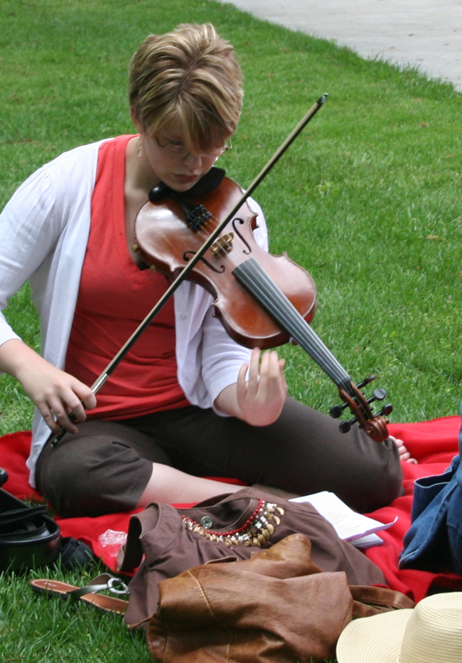 Woman sits on grass and tunes up her violin.