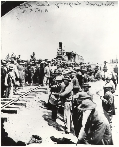 Train coming into Promontory Point, Utah. Black and white photo of a crowd standing around a train sitting on tracks