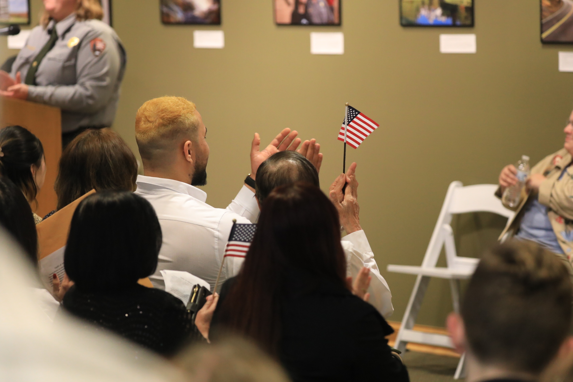People clap and two small US flags are waved. Woman in NPS uniform in back.