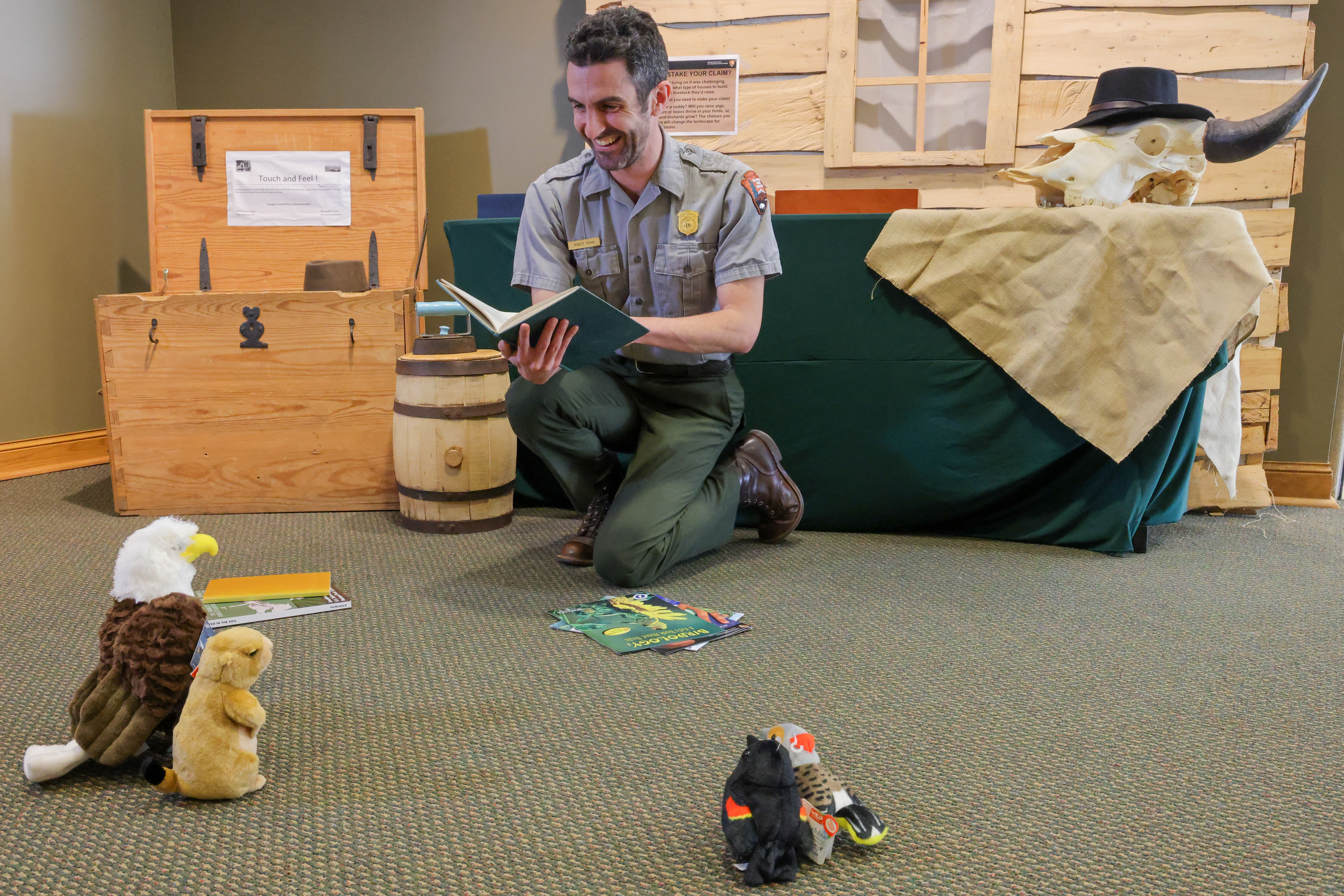 Uniformed park ranger reads indoors to audience of stuffed animals and bison head.