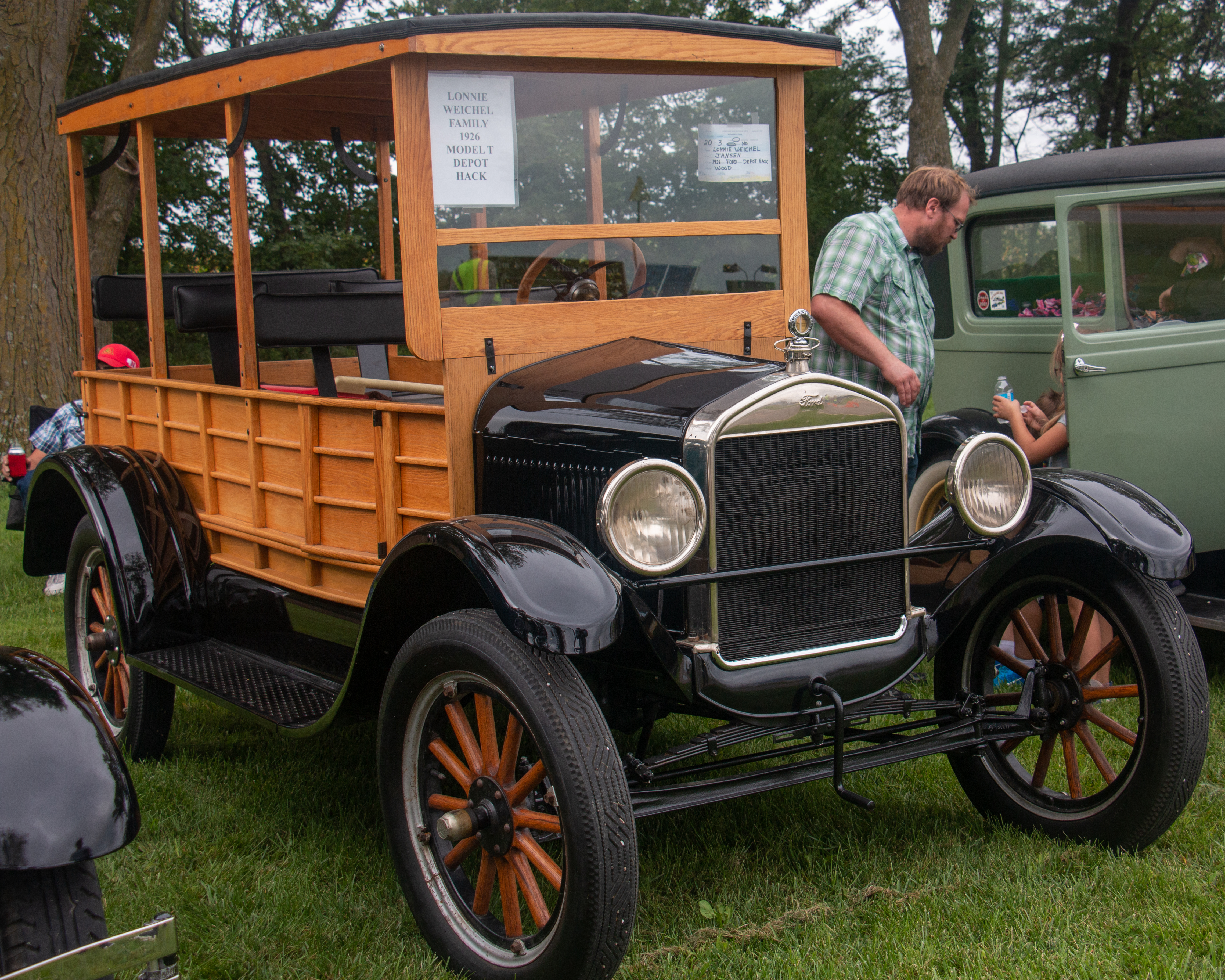 Homestead Era Car and Truck Show An old wagon-type car sits on grass. A man stands on the far side of the vehicle looking at the car next to it.