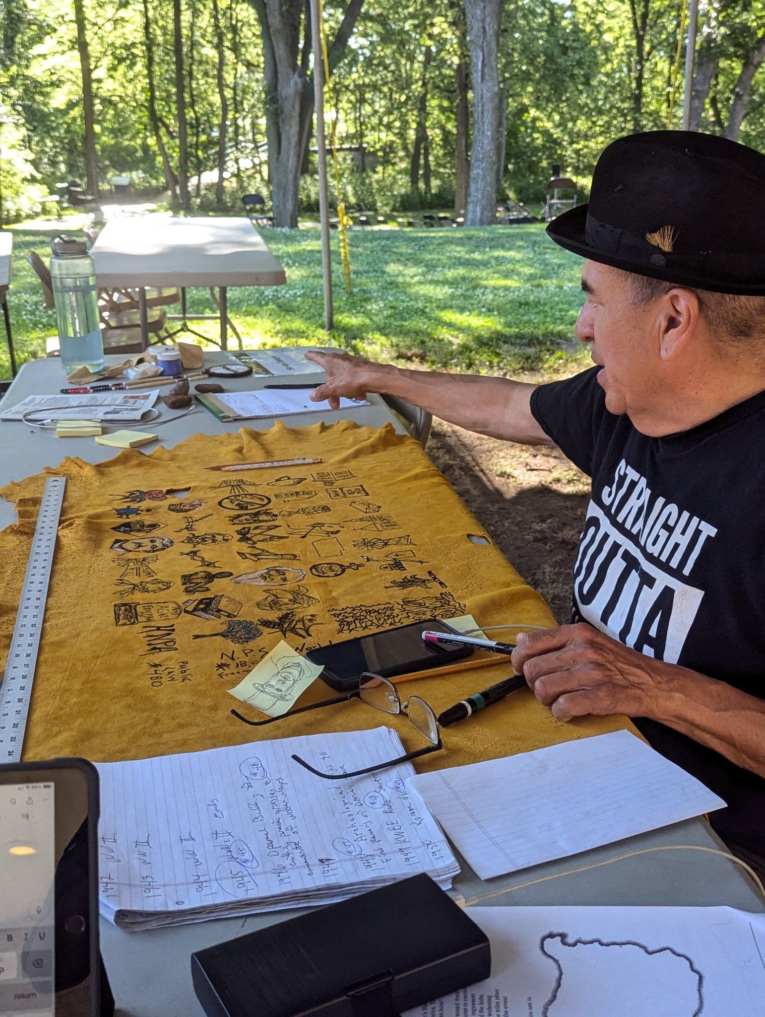 Traditional Sicangu Lakota artist, Steven Tamayo. Man with dark hat creates artistic calendar on softened deer skin in outdoor setting.