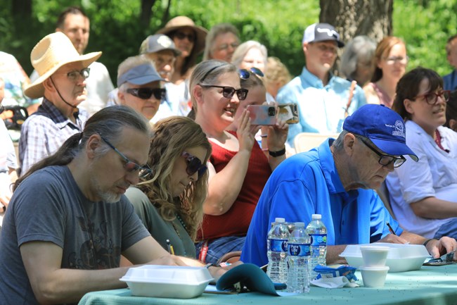 3 judges sit in the front row at fiddle fest. Audience claps behind them.