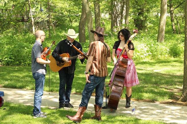 Four people holding musical instruments stand in a group on a sidewalk.