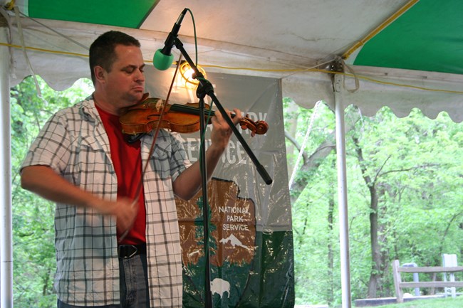 A man plays a fiddle in front of a microphone.